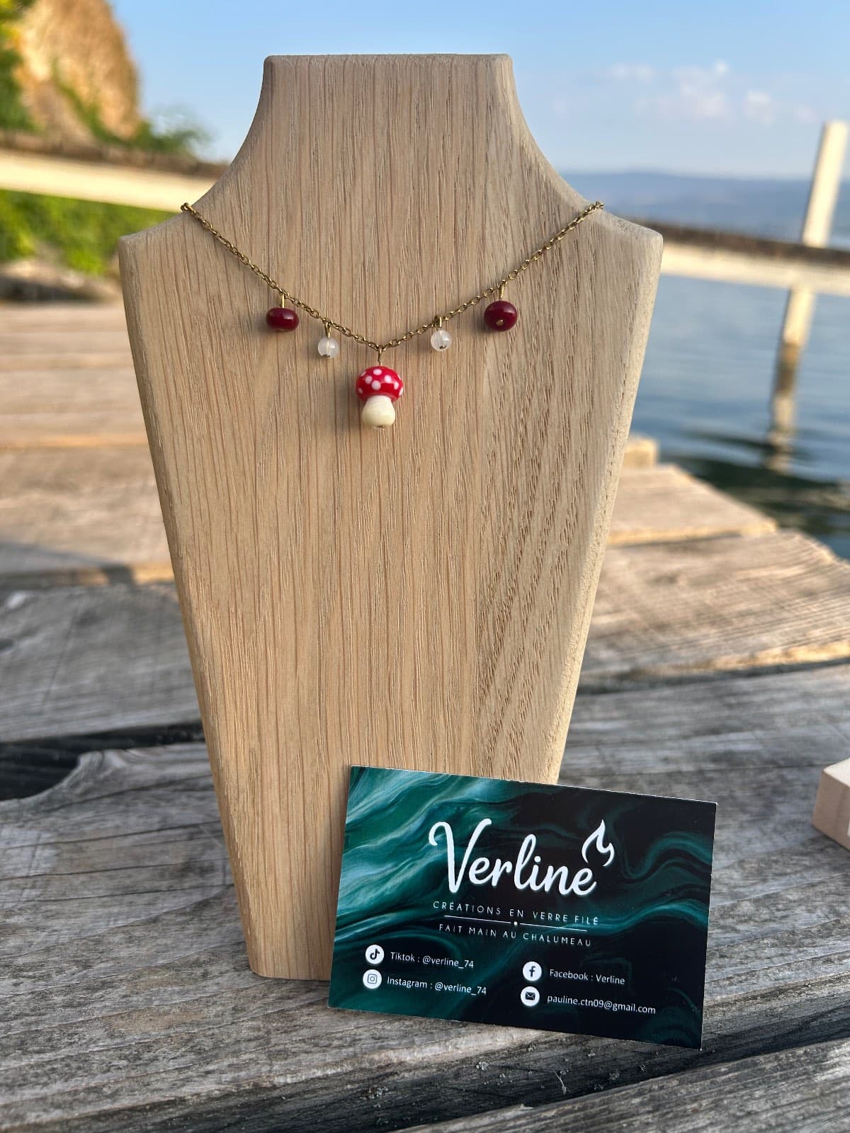 Buste en bois présentant le collier avec son pendentif champignon rouge et ses quatre perles suspendues.