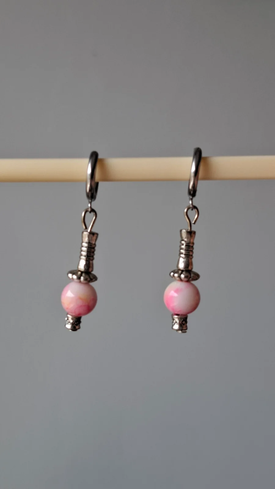 Boucles d'oreilles dormeuses avec perles roses et apprêts argentés posées sur une tranche de bois.
