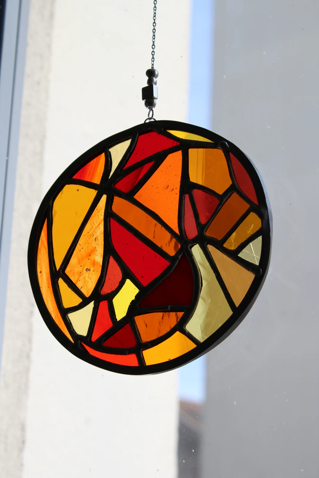 Suspension ronde en vitrail aux morceaux de verre déclinés en tons chauds orange et jaune traversés par la lumière.