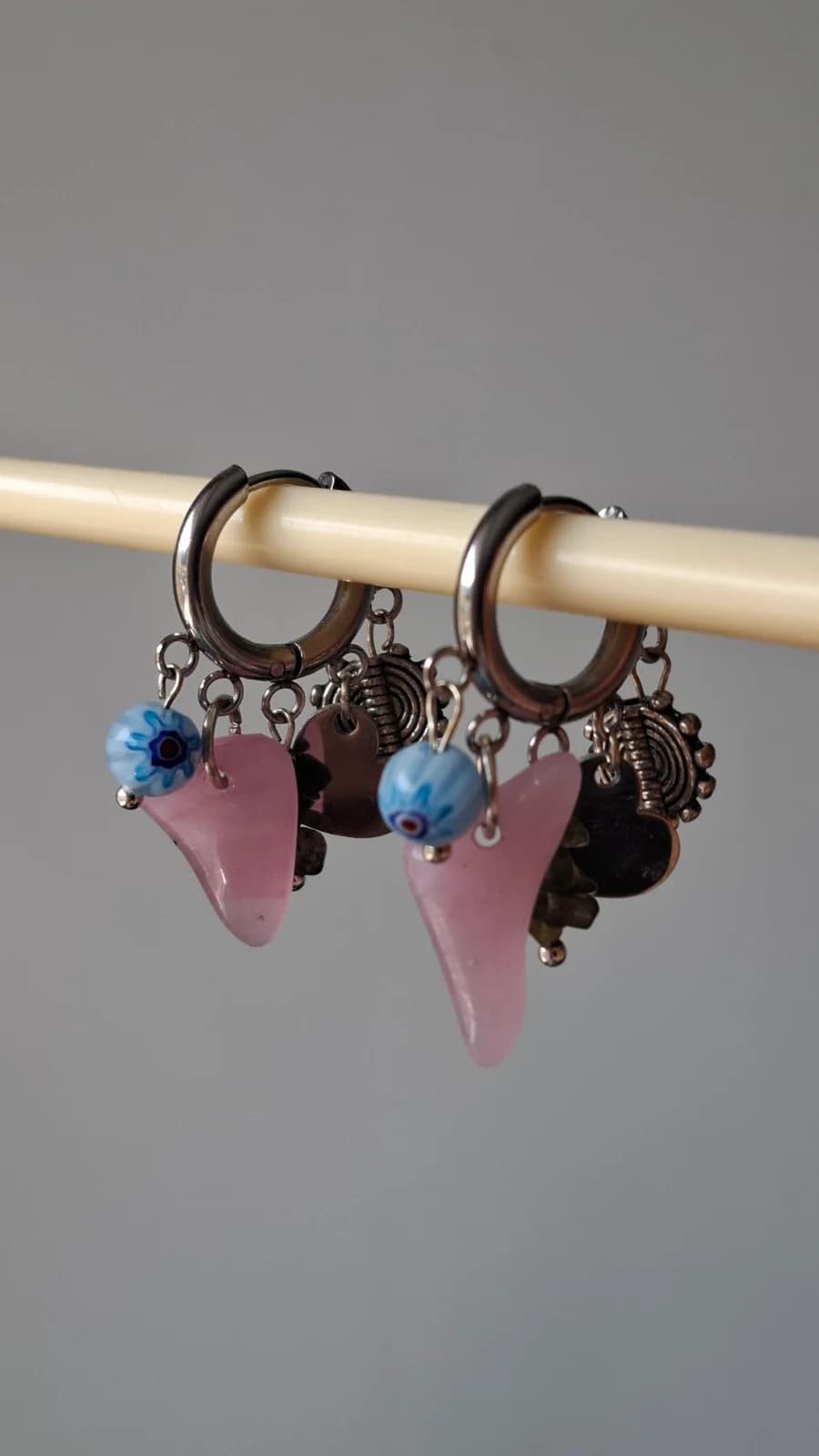 Paire de boucles d'oreilles en verre rose, perles et pampilles en métal posées à plat sur un support en bois