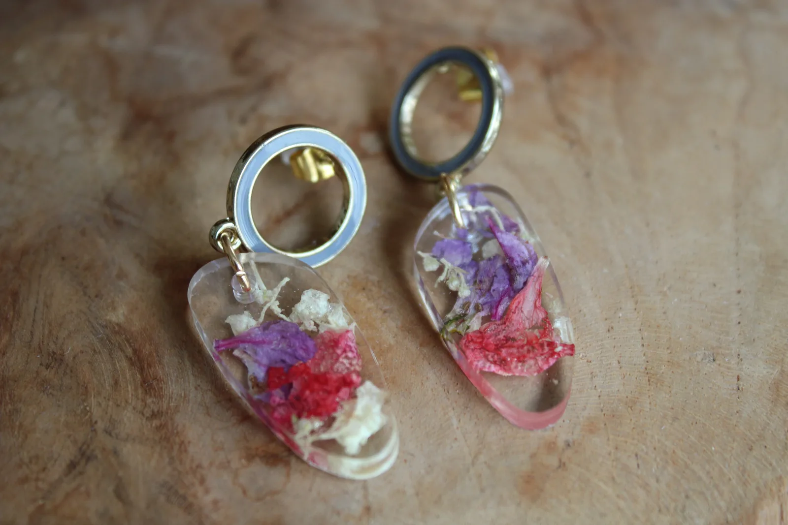 Vue rapprochée des boucles d'oreilles en résine transparente et fleurs séchées posées à plat sur du bois.