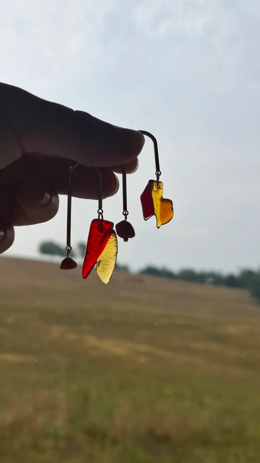 Paire de boucles d'oreilles dorées et verre rouge et ambré disposée sur un support en bois.