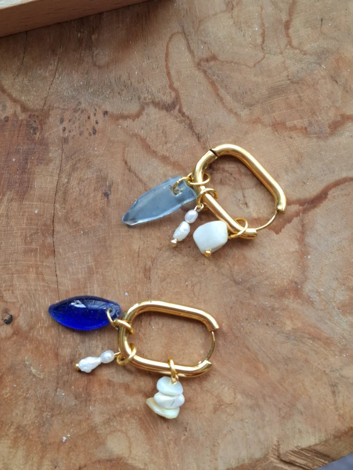 Boucles d'oreilles pendantes avec breloques en verre bleu et perles suspendues à un présentoir en métal.