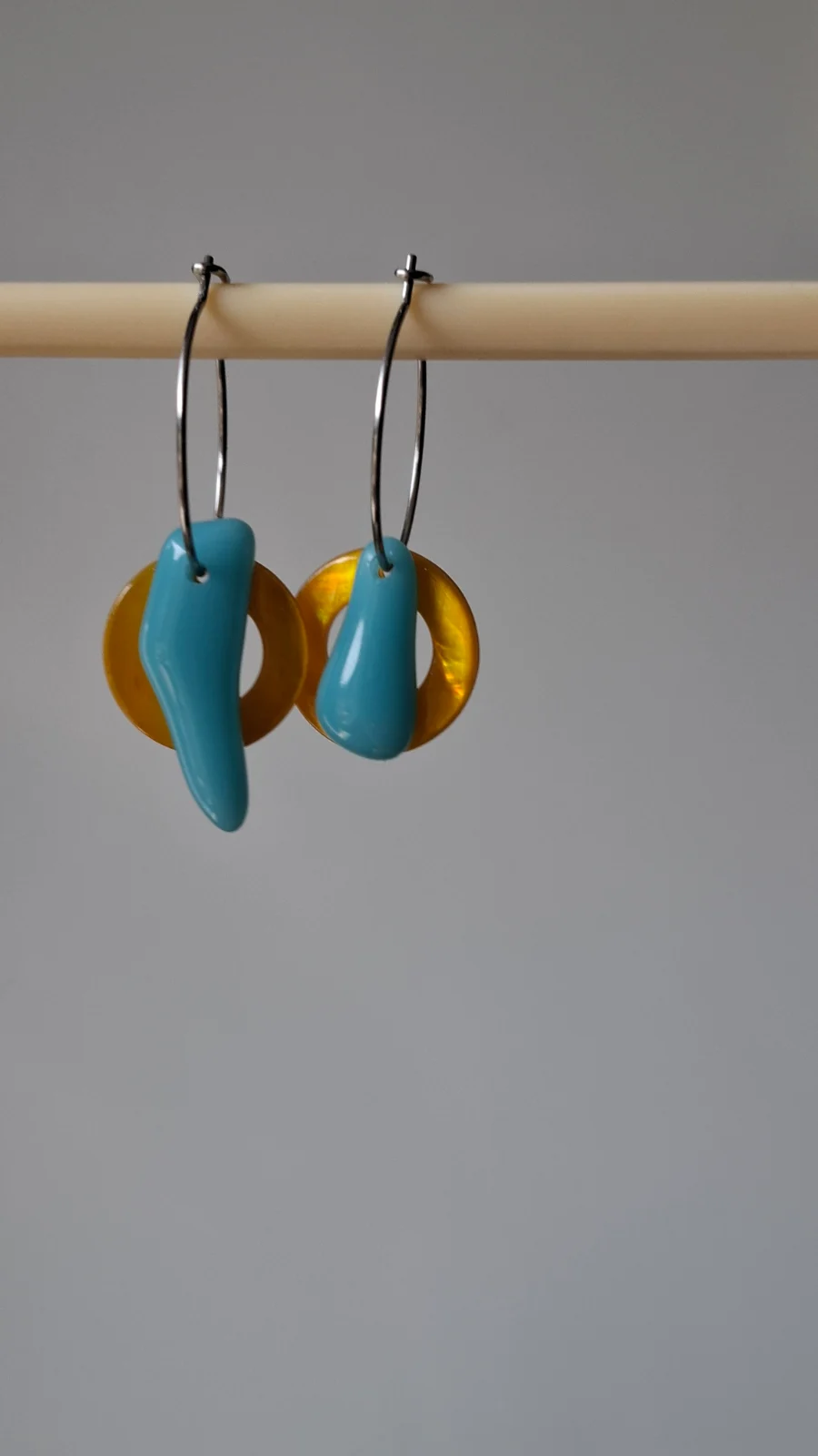 Paire de boucles d'oreilles à gouttes en verre bleu et anneaux jaunes posée sur un socle en bois.