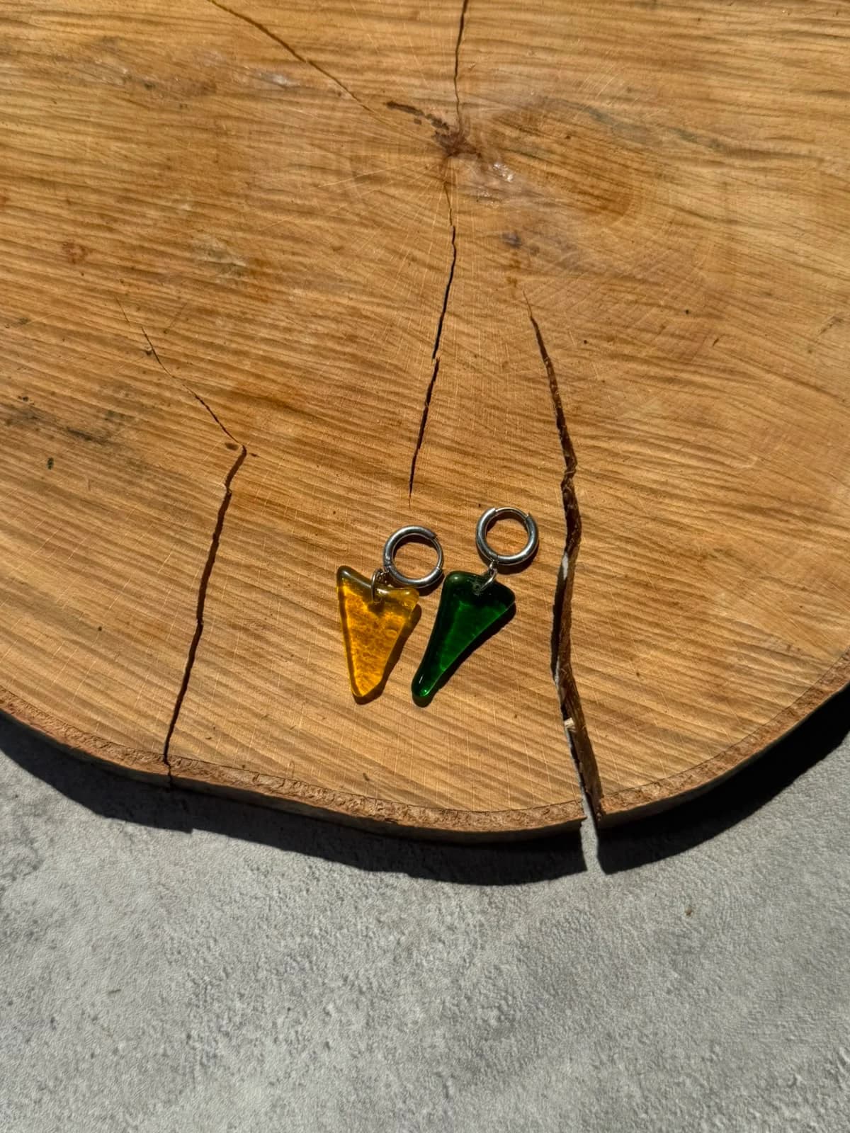 Main tenant deux boucles d'oreilles pendantes en verre jaune et vert translucides face à la lumière.