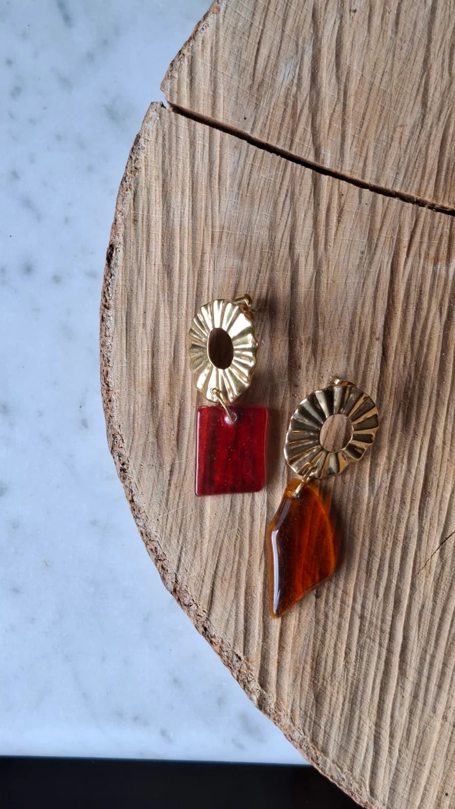 Boucles d'oreilles dorées et verre recyclé orange et rose posées sur un disque de bois.