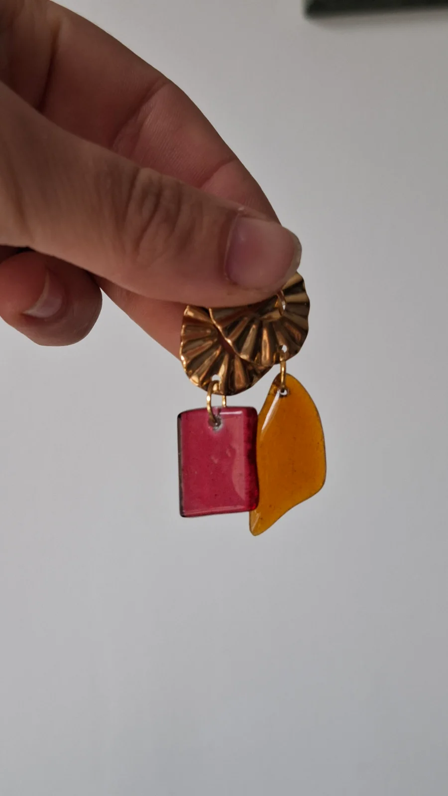 Pendentifs en verre translucide orange et rose tenus à la main en extérieur.