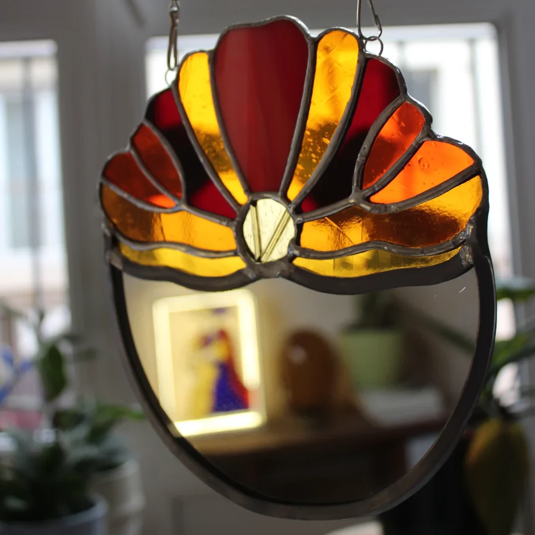 Miroir suspendu en vitrail Tiffany orné d'un motif en éventail aux verres jaune et orange.
