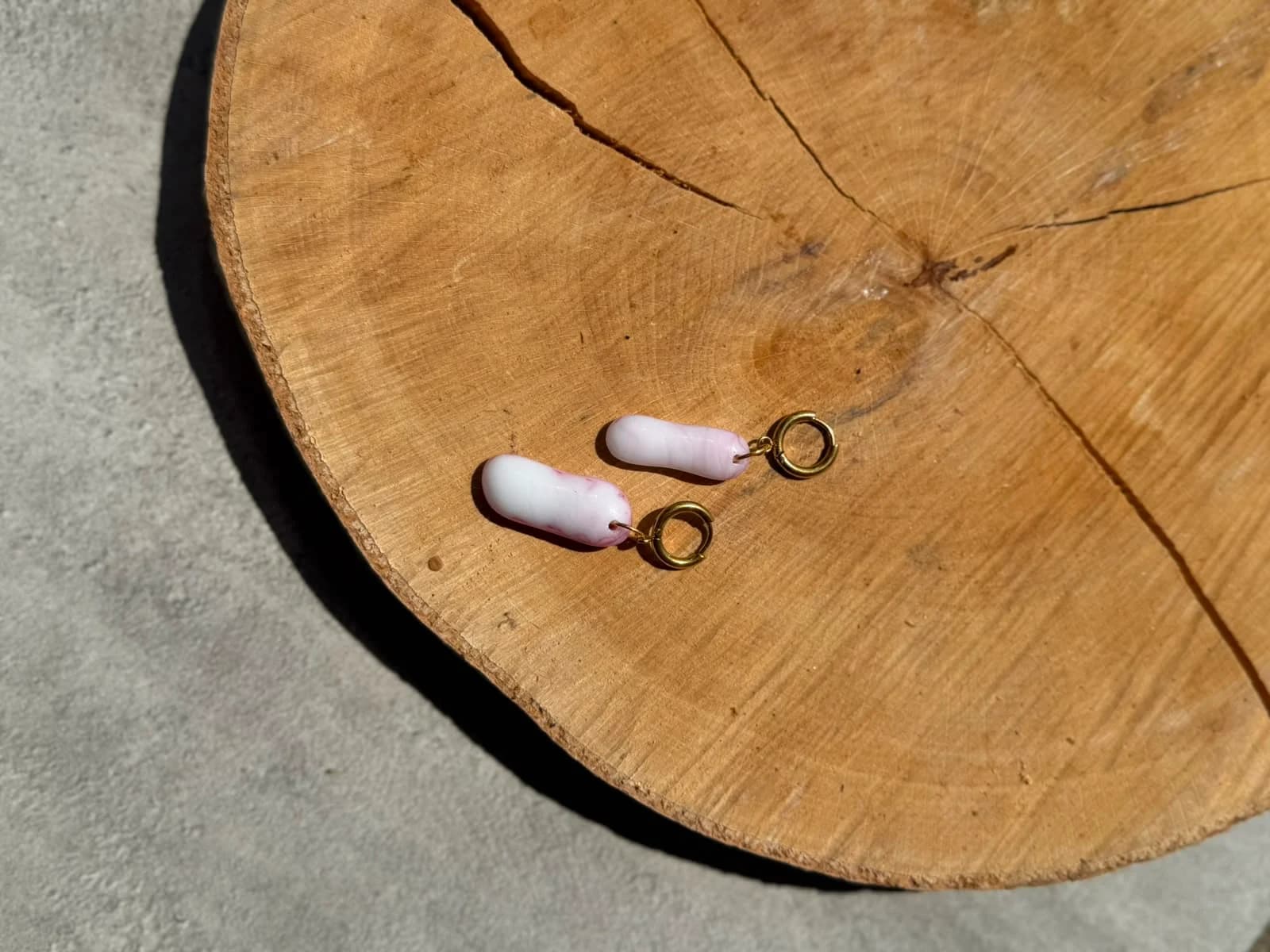 Boucles d'oreilles allongées en verre rose et blanc tenues à la main devant une plante.