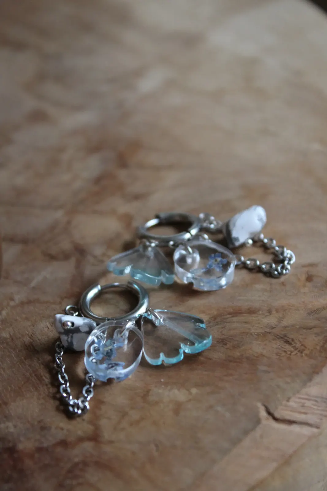 Paire de boucles d'oreilles créoles posée à plat sur un support en bois avec ses pendentifs floraux