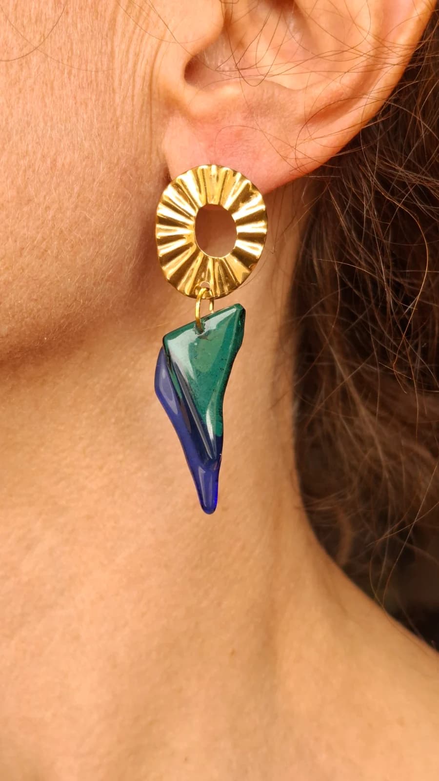 Boucle d'oreille portée avec puce ronde dorée et pendentif géométrique en verre bleu et turquoise.
