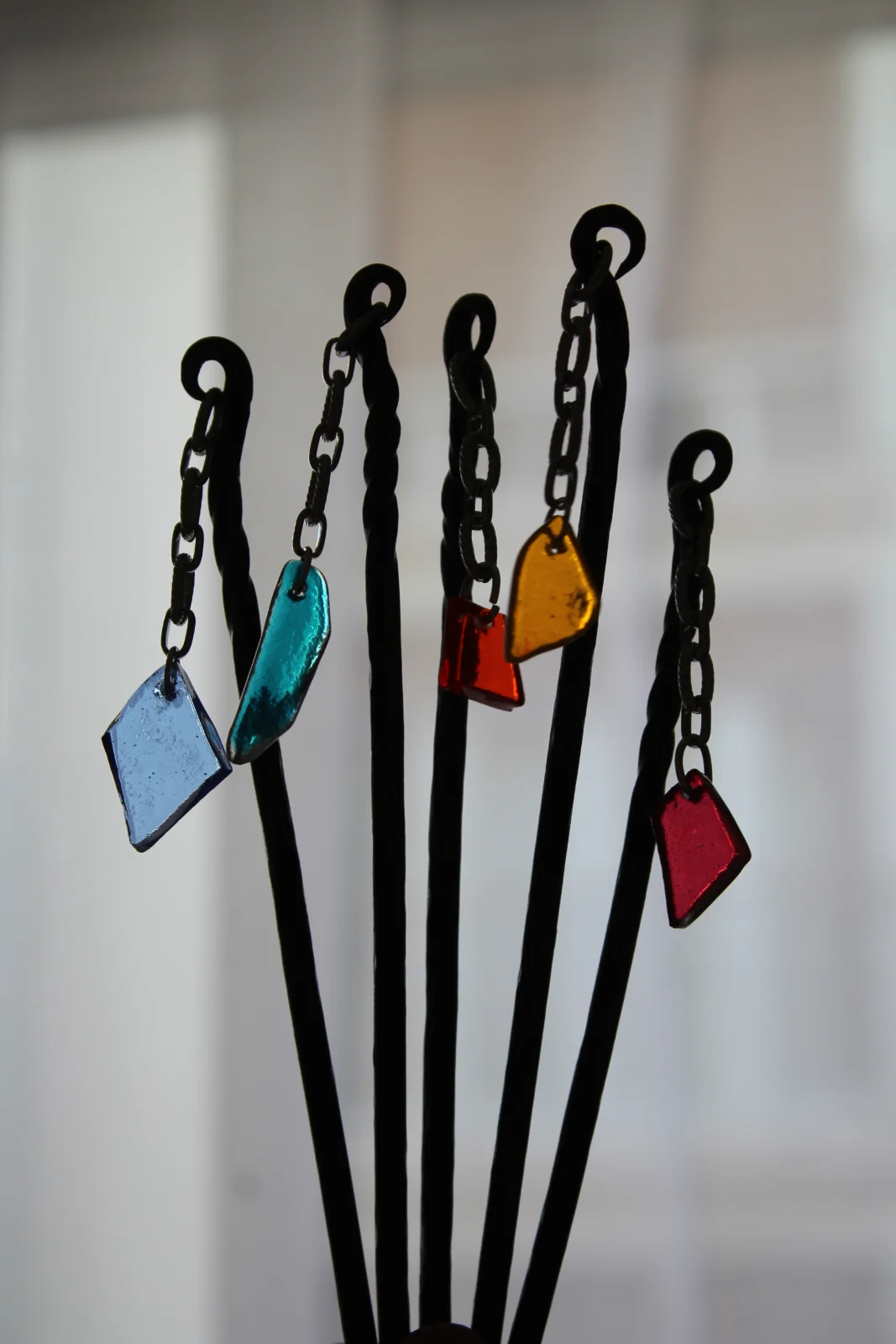 Piques à cheveux en métal noir forgé ornés de pendentifs en verre coloré bleu, jaune et rouge.