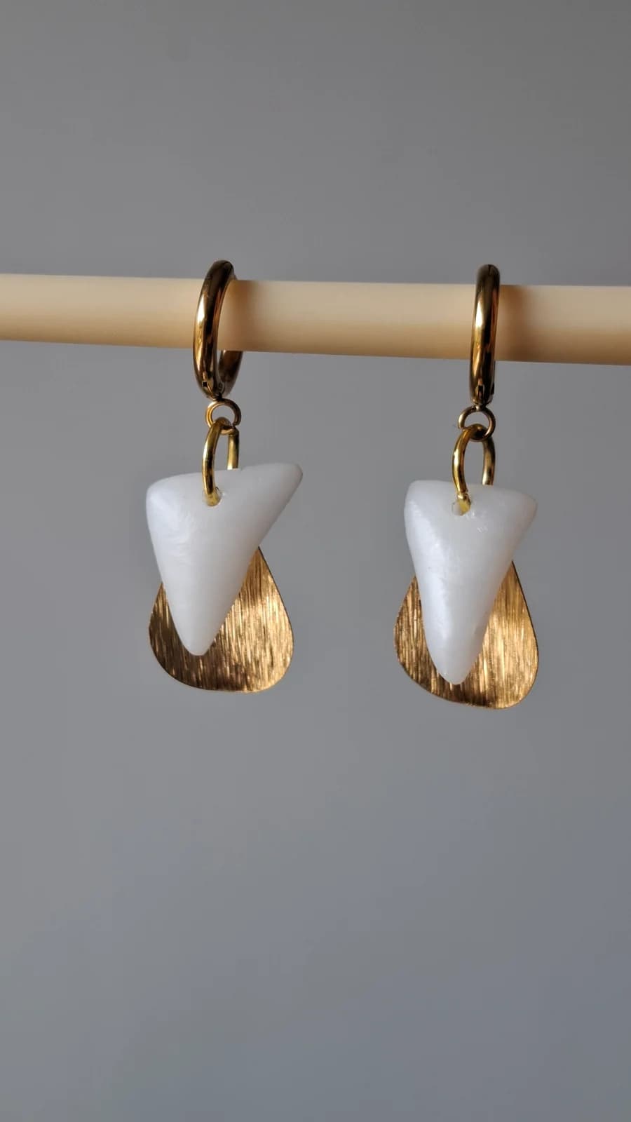 Paire de boucles d'oreilles pendantes en verre blanc et pampilles dorées suspendues sur un support.