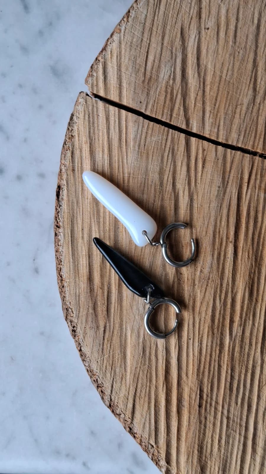 Paire de boucles d'oreilles avec pendentifs noir et blanc posée à plat sur une tranche de bois.