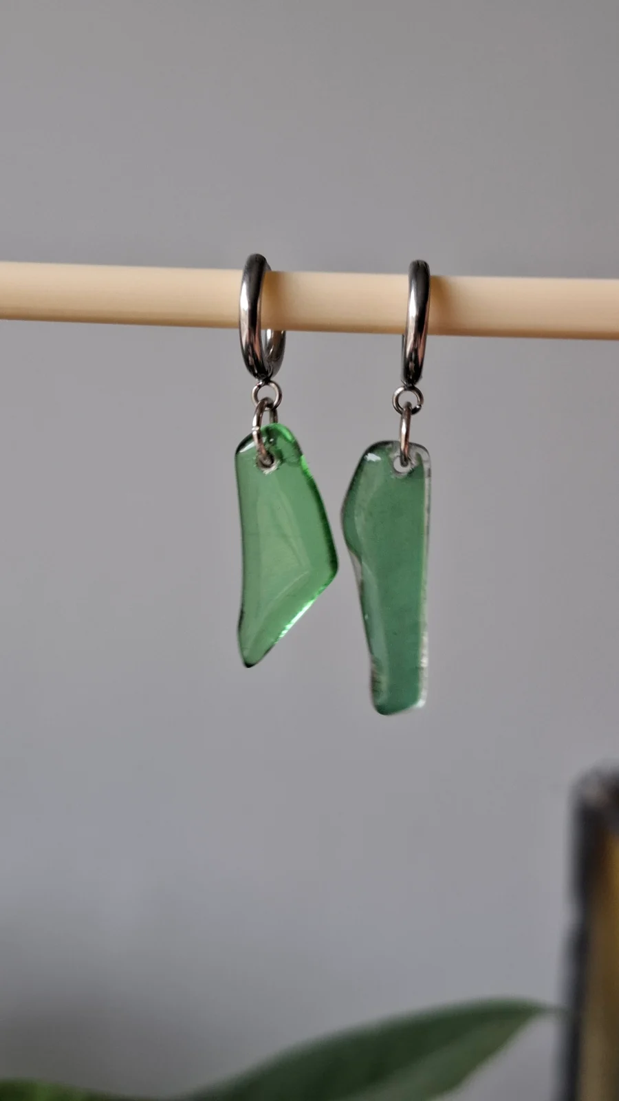Boucles d'oreilles pendantes en verre vert transparent suspendues sur une tige en bois.