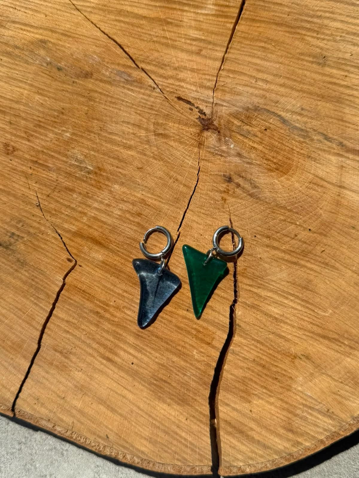 Boucles d’oreilles dormeuses avec pendentifs en verre bleu et vert posées sur une rondelle de bois.