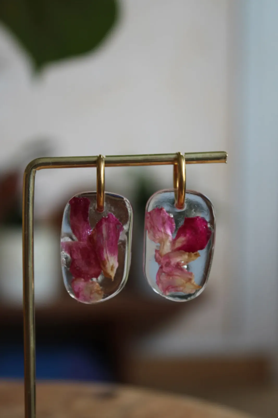 Paire de créoles dorées avec pendentifs en résine et fleurs séchées roses, présentées sur un support.