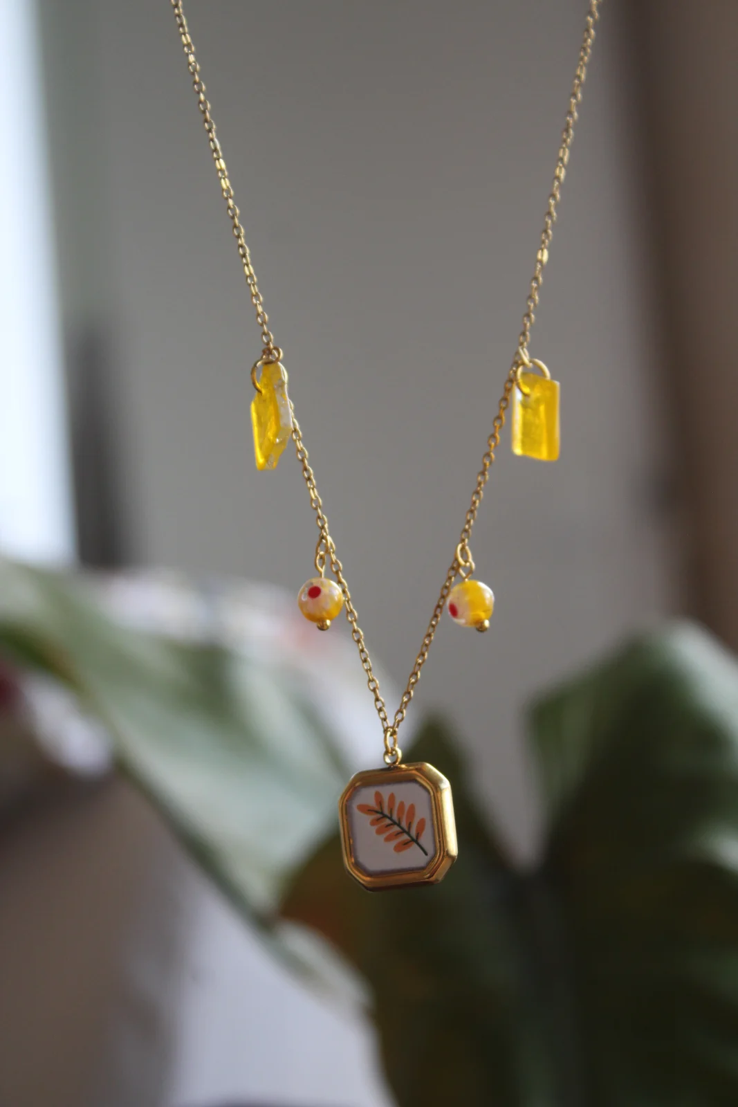 Gros plan sur le pendentif à motif de branche feuillue, pampilles et perles jaunes.