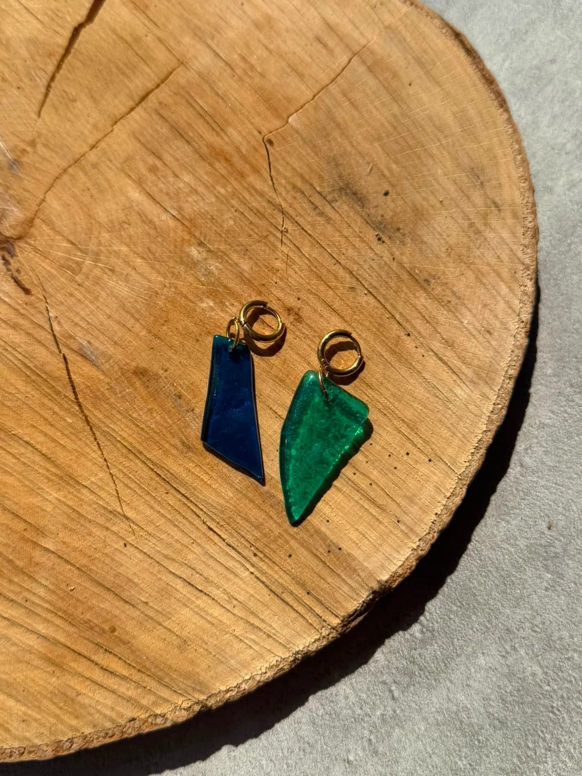 Paire de boucles d'oreilles en verre bleu roi et turquoise posée sur un socle en bois.