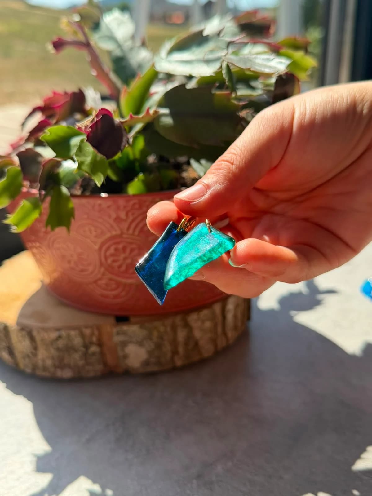 Boucles d'oreilles en verre bleu roi et turquoise tenues en main à la lumière naturelle.