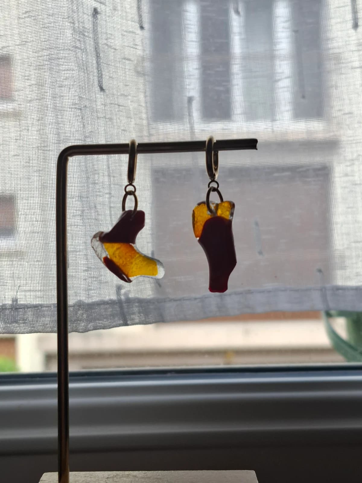 Boucles d'oreilles en verre jaune et rouge suspendues à un présentoir métallique devant une fenêtre