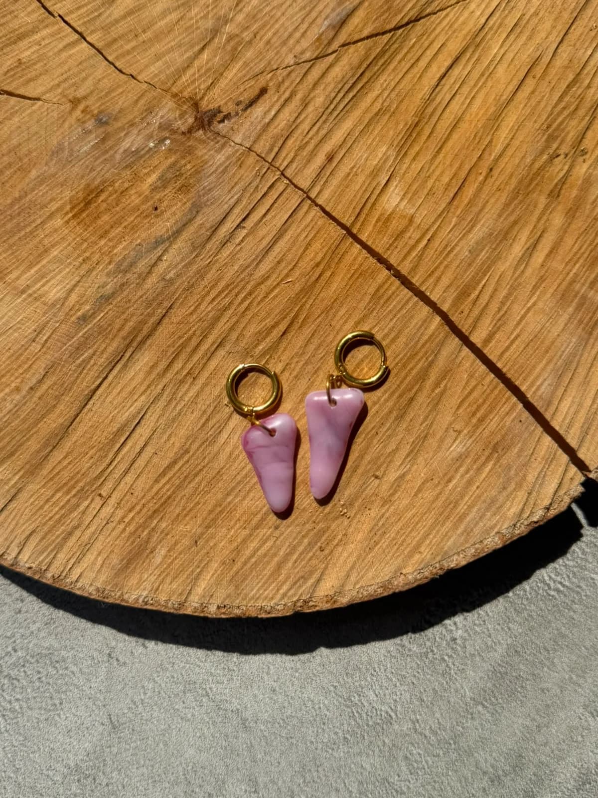 Paire de boucles d'oreilles en verre rose allongées posée à plat sur une tranche de bois.