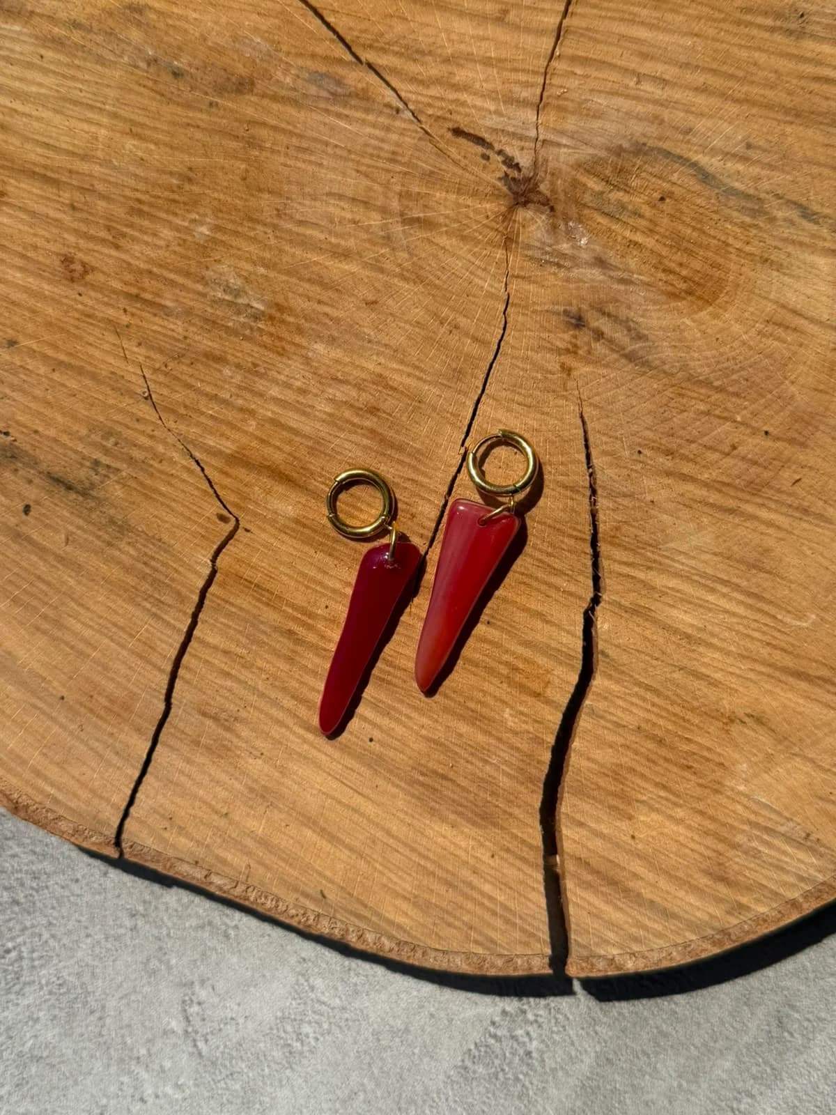 Boucles d'oreilles pendantes en verre rouge montées sur dormeuses dorées, disposées sur un rondin de bois.