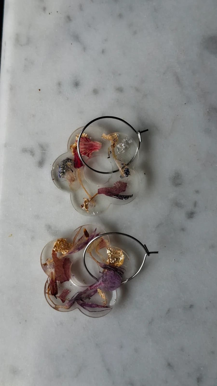 Créoles et pendentifs fleurs en résine transparente avec fleurs séchées et dorures sur marbre.