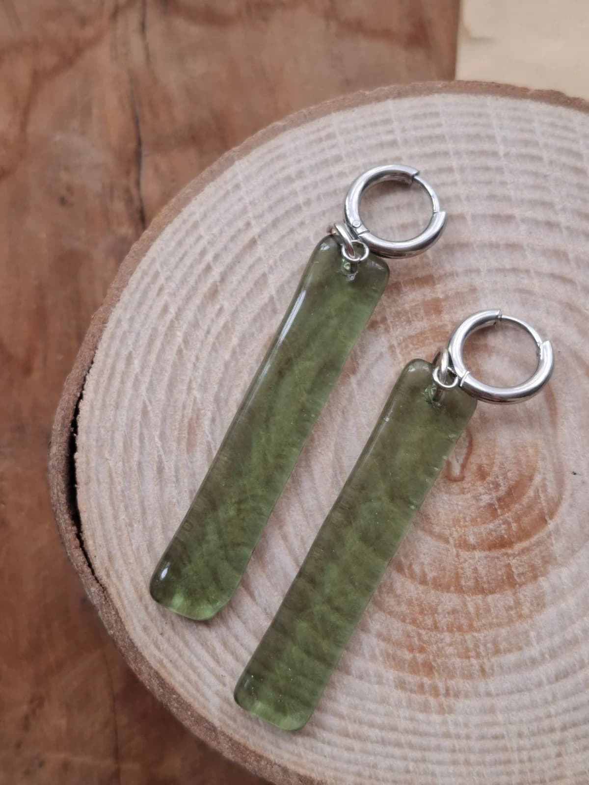 Boucles d'oreilles pendantes rectangulaires en verre vert translucide suspendues à une tige en bois.