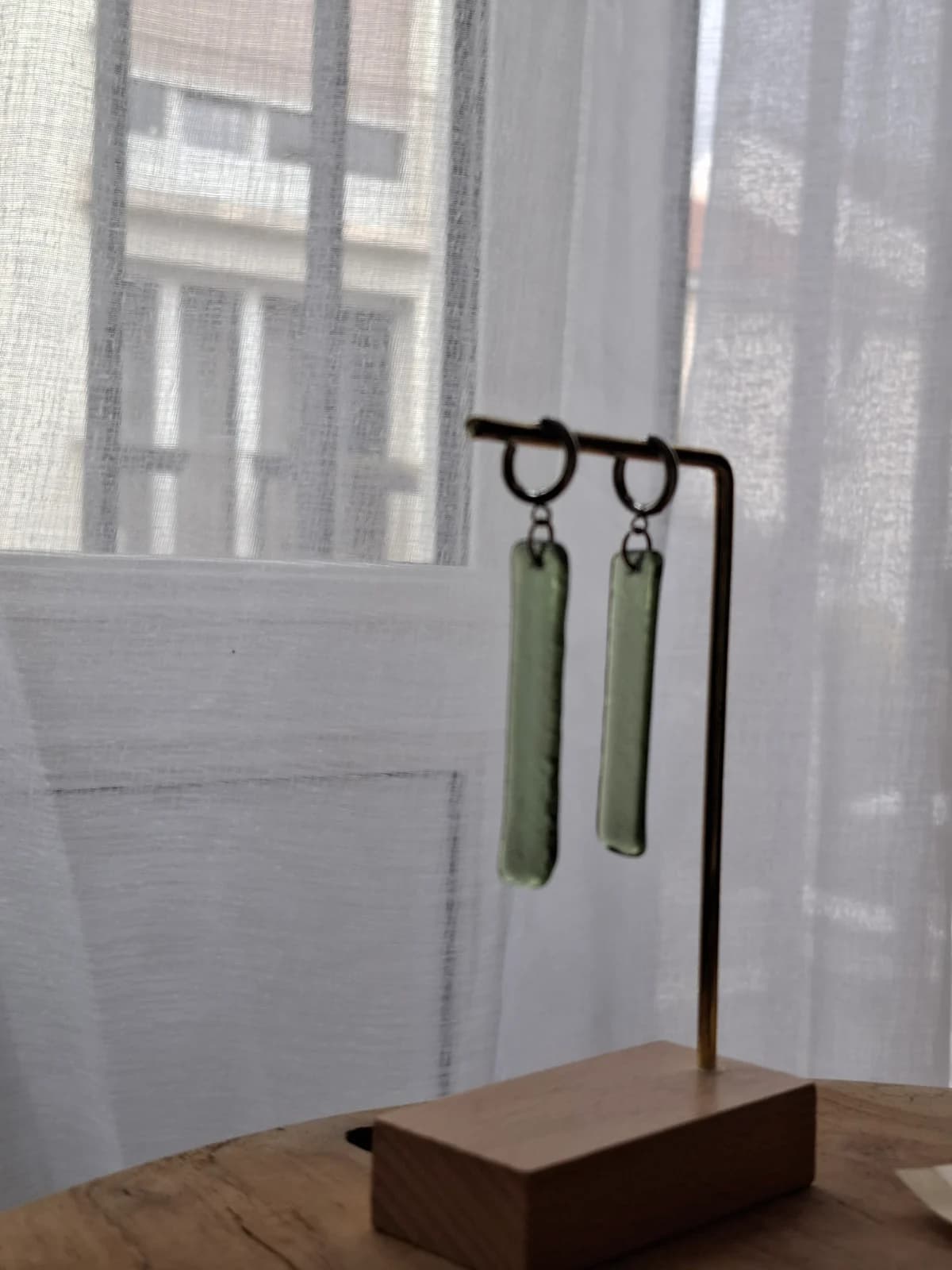 Boucles d'oreilles rectangulaires en verre vert avec anneaux argentés posées sur une rondelle de bois.