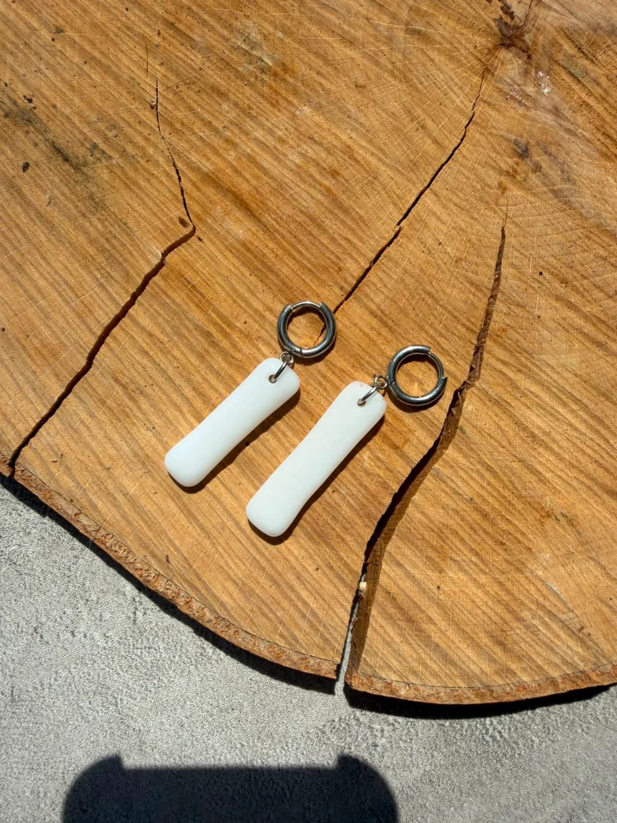 Boucles d'oreilles rectangulaires en verre blanc présentées à plat sur un rondin de bois.