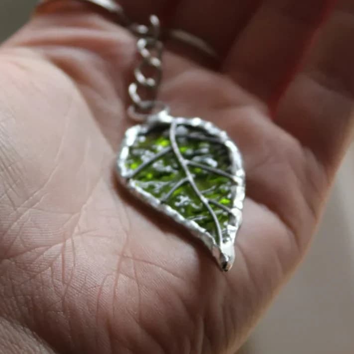 Porte-clés feuille en vitrail vert texturé et métal argenté tenu dans une main.