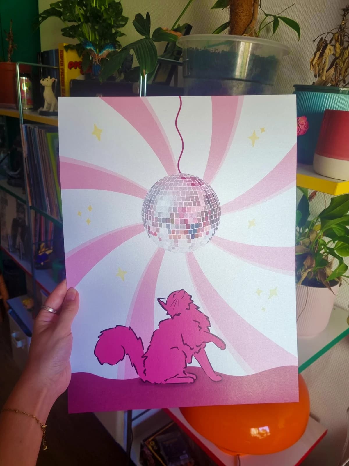 Affiche graphique avec chat rose observant une boule à facettes sur fond rayonnant rose et blanc.
