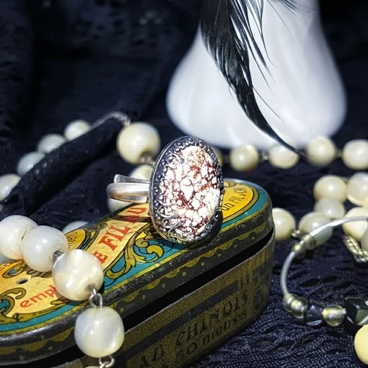 Bague réglable en argent et magnétite ovale posée sur une boîte vintage décorée.
