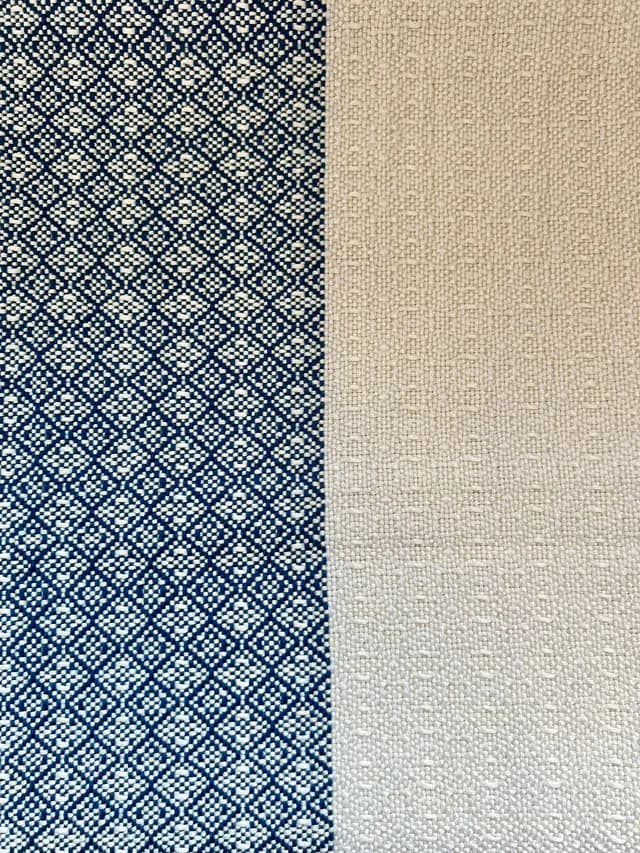 Gros plan sur le tissage artisanal bicolore aux motifs géométriques bleus et texture écrue.