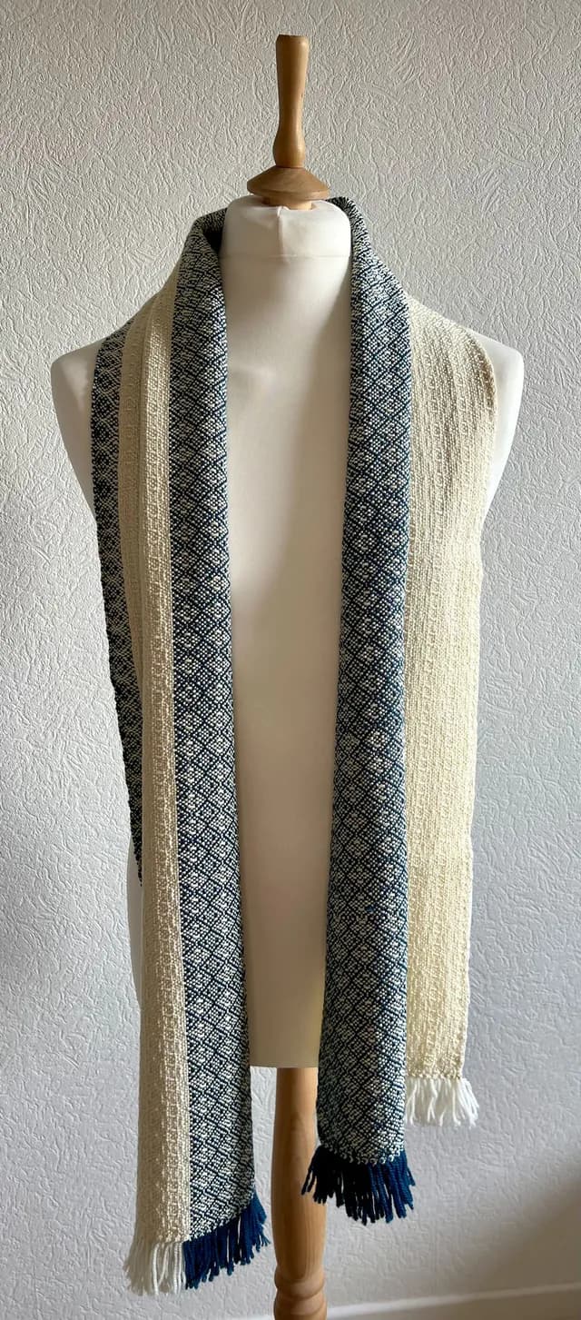 Écharpe bicolore bleu et écru à motifs géométriques drapée sur un buste de mannequin avec franges.