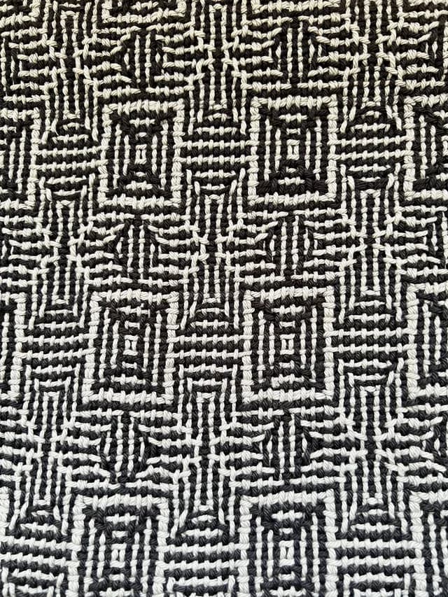 Gros plan sur le tissage artisanal géométrique aux fils noirs et gris.