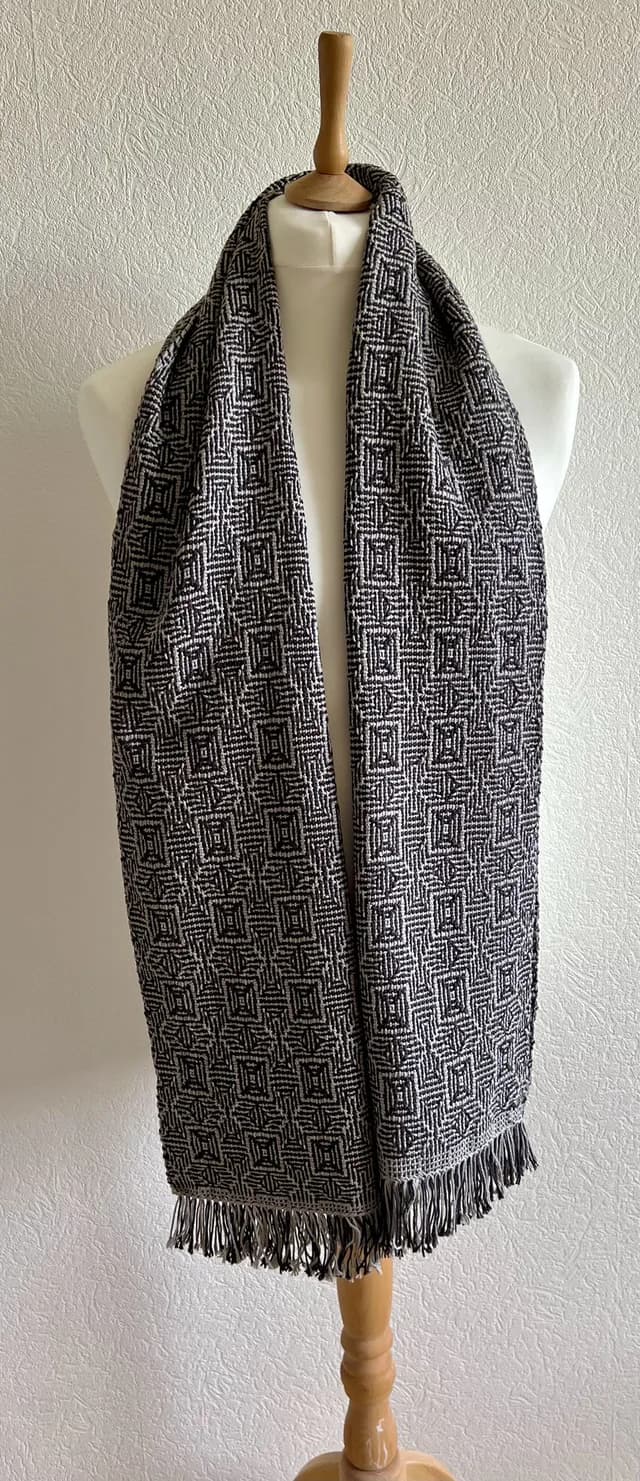 Écharpe tissée à motifs géométriques noir et gris à franges, portée sur un buste de mannequin.