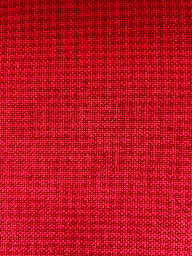 Gros plan sur la texture serrée et le maillage d'un tissu artisanal rouge.