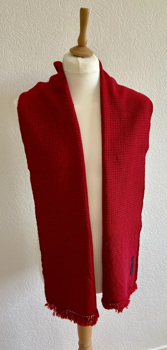 Écharpe rouge tissée à petites franges disposée sur un buste de mannequin blanc.