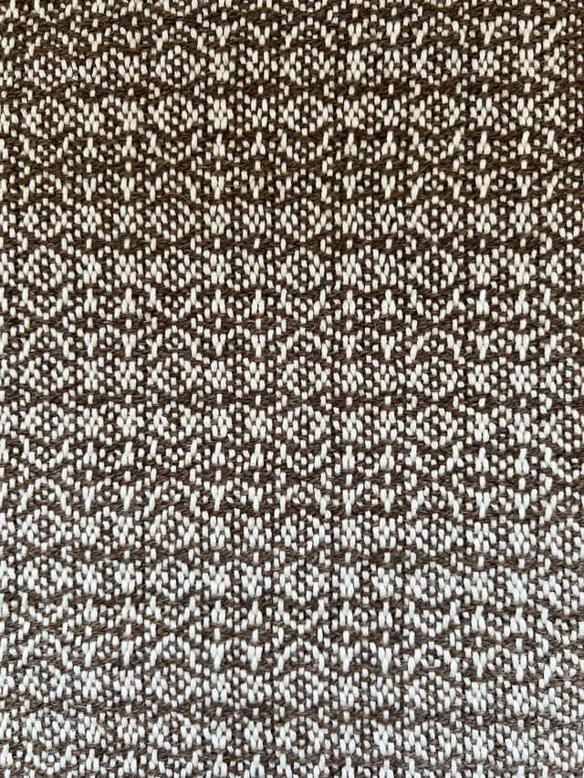 Gros plan sur les motifs géométriques du tissage artisanal marron et blanc.