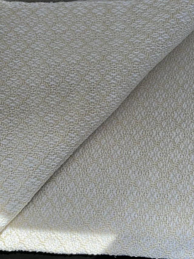 Plaid pour bébé tissé écru et beige aux motifs géométriques, délicatement replié.