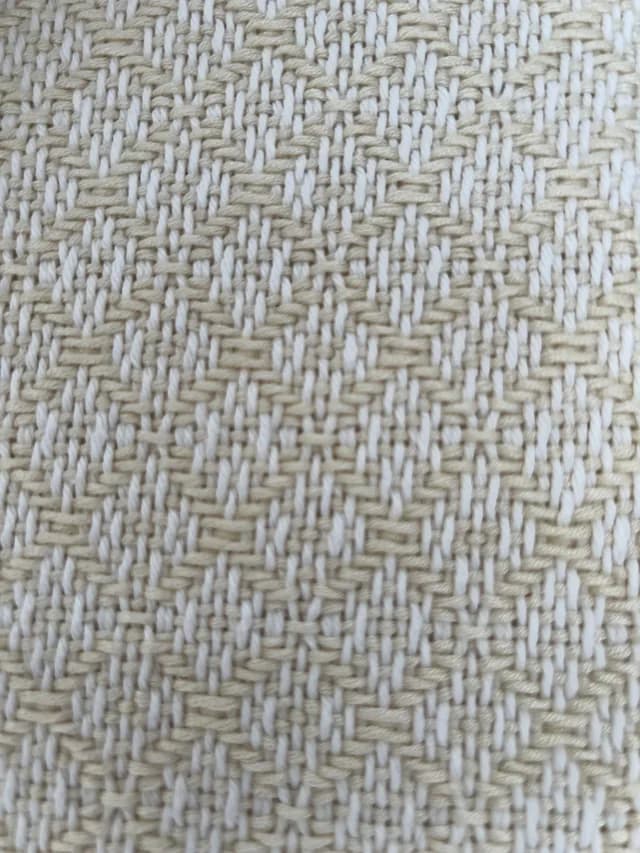 Gros plan sur le tissage texturé aux fils beiges et blancs formant des motifs géométriques.