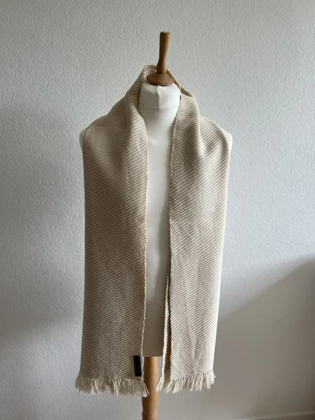 Écharpe tissée beige champagne à fines franges portée sur un buste de mannequin.