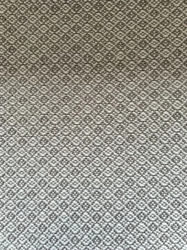 Gros plan sur le tissage texturé bicolore gris et blanc à motif de petits losanges.