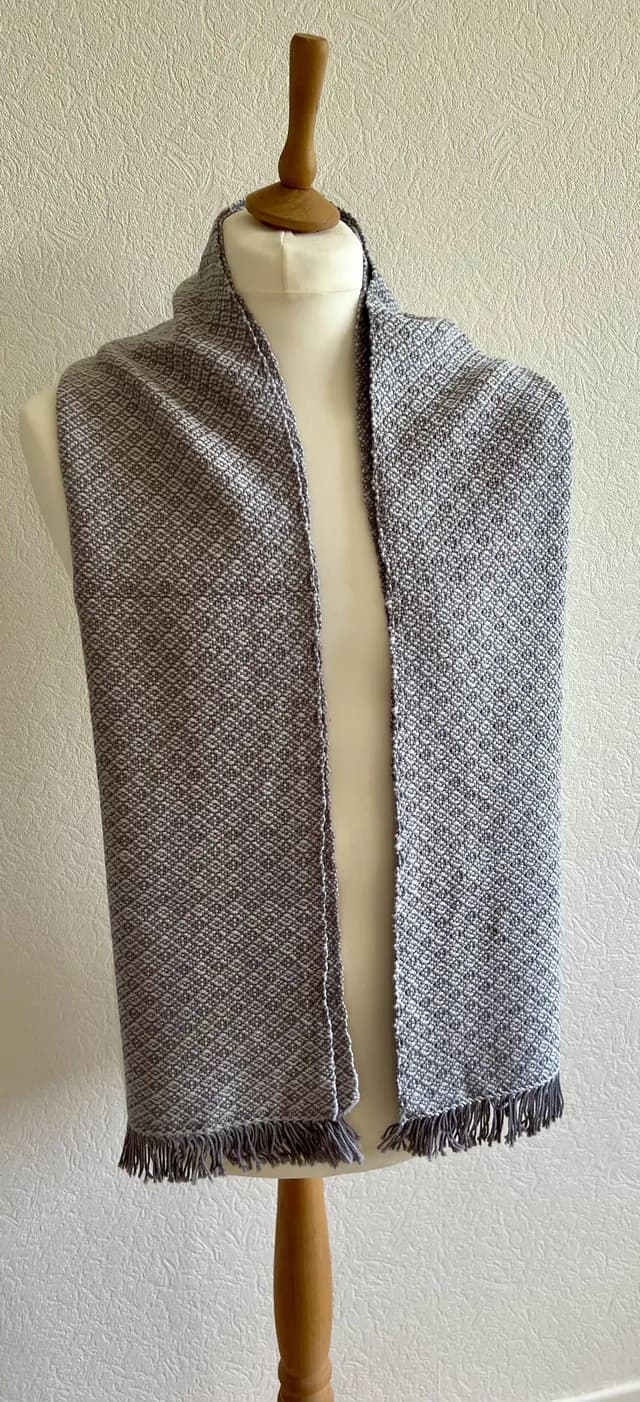 Écharpe tissée gris clair à motifs géométriques avec franges, portée sur un buste de mannequin.
