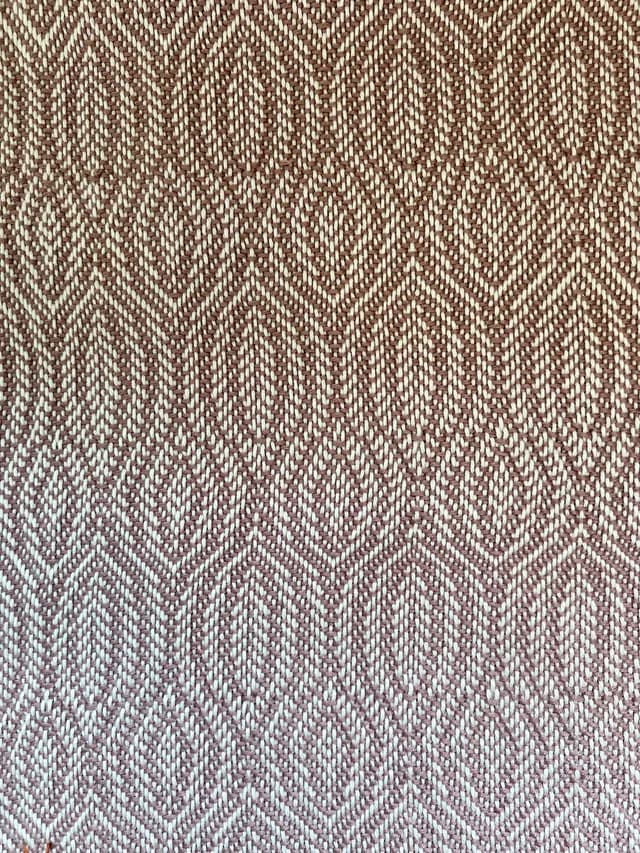 Gros plan sur le tissage géométrique à losanges dans les tons vieux rose et blanc cassé.