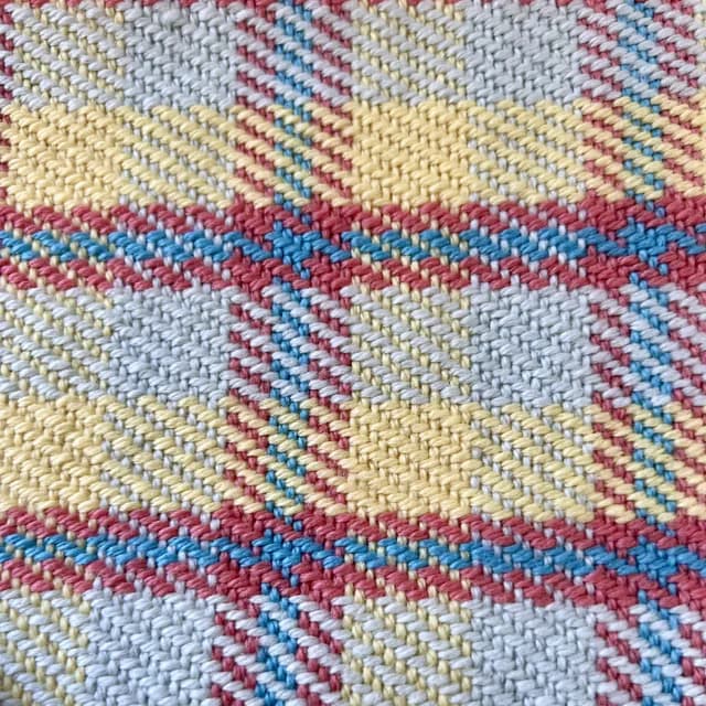 Gros plan sur le tissage artisanal à motif tartan aux fils jaunes, bleus, roses et blancs