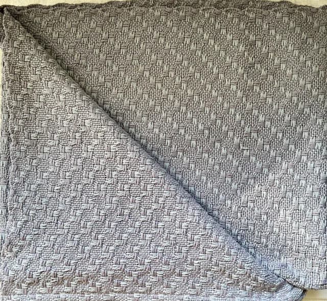Plaid en coton tissé à la main plié avec relief texturé gris clair.