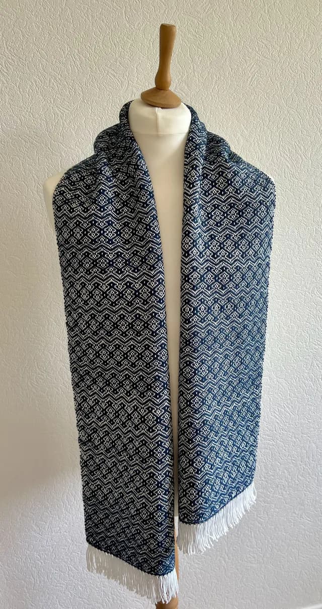 Écharpe tissée à motifs géométriques bleus et blancs avec franges, disposée sur un mannequin